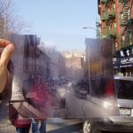 someone standing in a street in nyc, holding up a transparent photograph of the same street at a different time