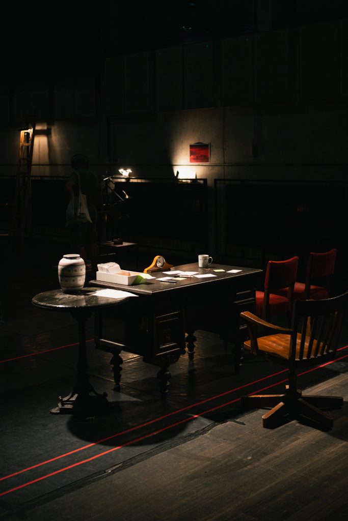 a desk dimly lit. in the background some objects, also dimly lit