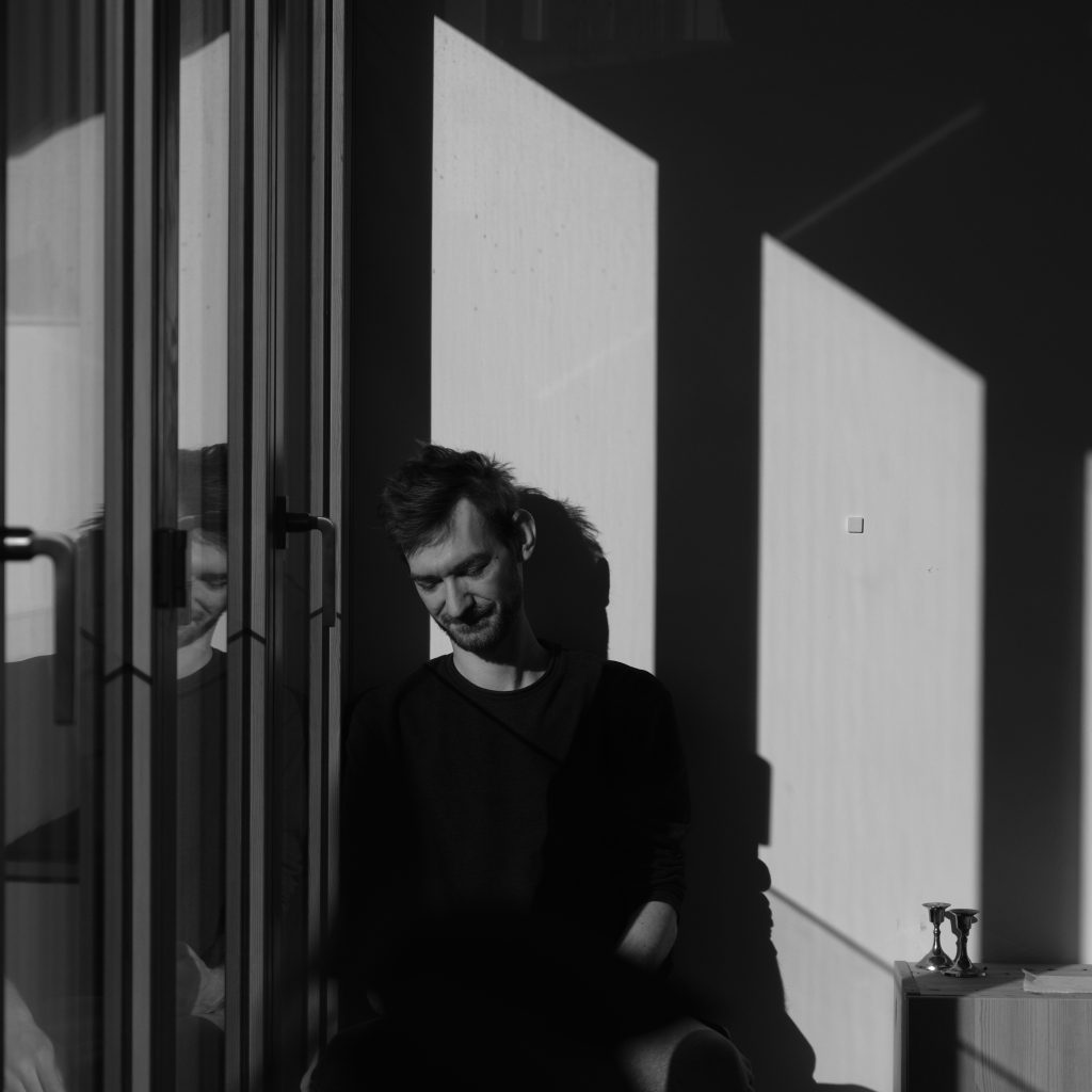a high contrast black and white image of a white man (philipp ehmann) in his 30s next to a window looking at the floor